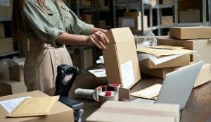 Female small business owner packing ecommerce order package in box at table.
